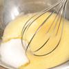 Đánh đều trứng trong bát cho đến khi trứng có màu vàng sáng. Từ từ thêm đường vào, trộn tiếp. Rây bột mì vào bát trứng. Sau đó, trộn cho đến khi hỗn hợp hòa quyện với nhau.