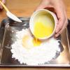 Trứng đập ra bát, dùng đũa đánh tan. Đổ bột ra khay rộng, thêm đường, nước, dầu, trứng và baking soda