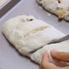 Khi bột đã thành khối dẻo mịn thì nhẹ nhàng dùng tay dàn mỏng, cho hạt óc chó cùng trái cây khô vào lòng bột và cuộn tròn lại. Sau đó chia bột thành hai phần bằng nhau rồi tạo thành khối dài như hình thoi cho hai khối bột. Lót giấy nến lên khay nướng, cho bánh lên, lấy dao khứa vài đường chéo trên mặt bánh và ủ cho bột nở to. Mở lò trước ở 220 độ C, sau đó cho khay bánh vào nướng 22 - 24 phút. Bánh chín vàng giòn thì lấy ra, đợi nguội một chút là có thể dùng.