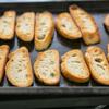 Dùng da cắt bánh mì thành từng miếng có kích thước bằng nhau, quết dầu olive lên 2 mặt của bánh mì, cho vào lò nướng ở nhiệt độ 230 độ C trong 5-6 phút hoặc cho đến khi 2 mặt bánh mì vàng đều.