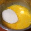 Cho 2 lòng đỏ trứng vào âu cùng với 50g đường cát (chia làm 3 lần), dùng máy đánh trứng đánh cho đến khi đường tan thì thêm vào 1 quả trứng nữa, tiếp tục đánh bông cho đến khi hỗn hợp mịn mượt, chuyển màu vàng nhạt. 