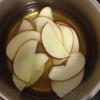 Cho 500ml nước táo ép và 200g đường vào nồi, nấu cho tan đường và từ từ cho lần lượt một ít táo đã cắt lát vào trụng sơ. Đến khi lát táo hơi mềm cảm thấy không còn giòn nữa và có thể uốn cong thì vớt ra.