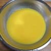 Khuấy tan 85g đường trắng với 100 ml sữa tươi rồi cho 2 trứng gà, 2 giọt màu vàng thực phẩm vào, đánh tan đều rồi lọc qua rây cho mịn.
