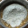 Cho chuối cắt nhỏ vào. Rây bột mì, bột nở, baking soda vào bát, dùng phới trộn cho bột và trứng hòa quyện với nhau.