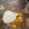 Sau tách xoài xong, bạn cho các miếng xoài vào máy xay sinh tố. Dùng muỗng đong 100ml sữa tươi và 30ml sữa chua rồi đổ vào máy chung với xoài và xay cho tới khi có được nước xoài mịn mượt như thế này.